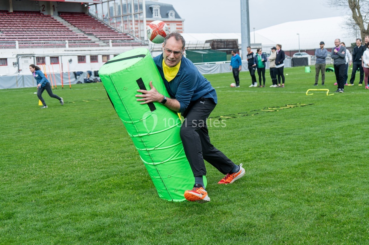 Un homme s'entraîne au rugby en plaquant un sac de plaquage vert sur un terrain en herbe.