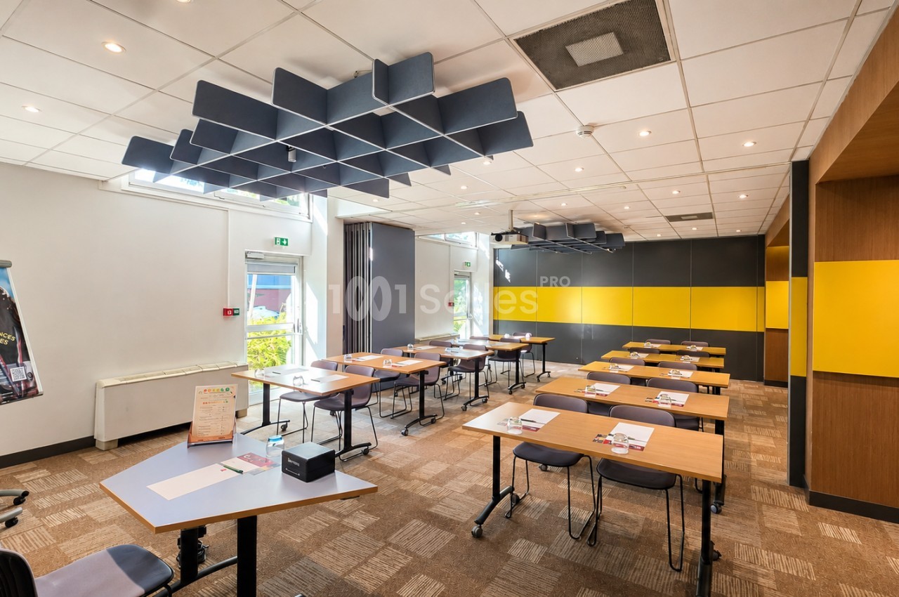 Salle de réunion modulaire avec tables en bois, chaises noires, panneaux acoustiques bleus au plafond et cloison jaune.