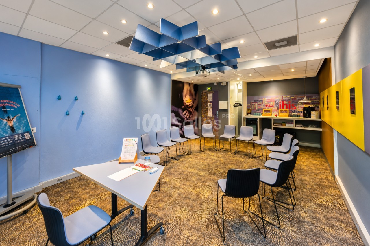Salle de réunion moderne avec murs bleu et jaune, chaises blanches et noires, faux plafond acoustique bleu.