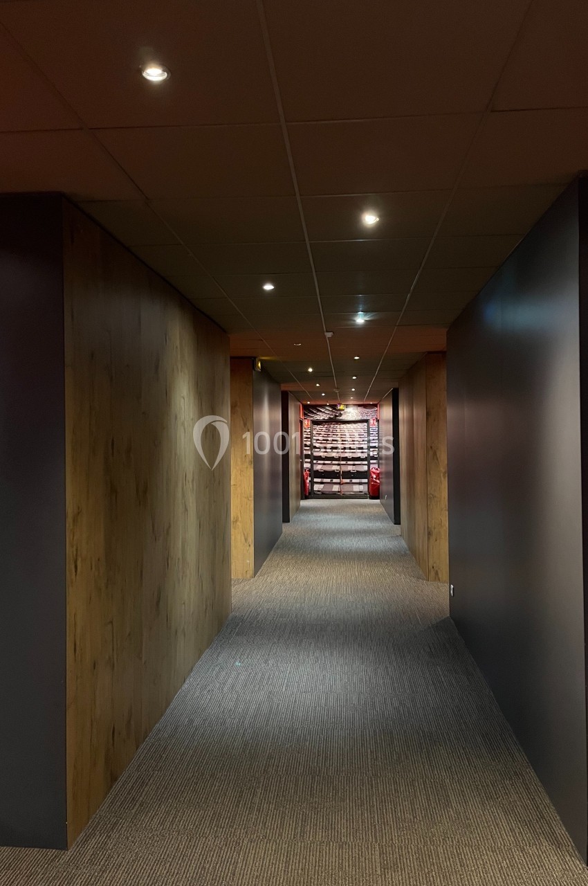 Couloir moderne avec murs en bois et éclairage tamisé, menant à une structure métallique rouge visible au fond.