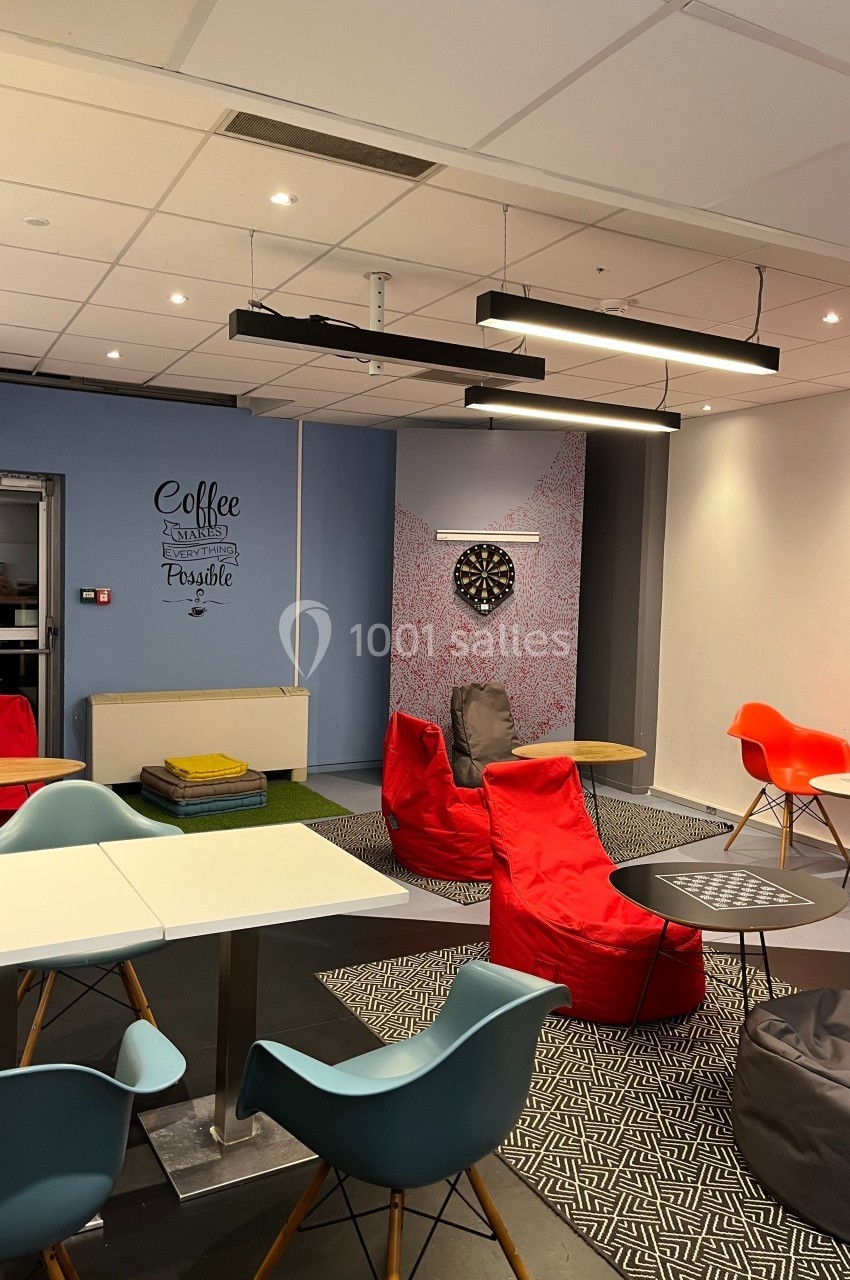 Espace détente avec fauteuils colorés, poufs, table de jeux, cible de fléchettes et décoration murale inspirante.