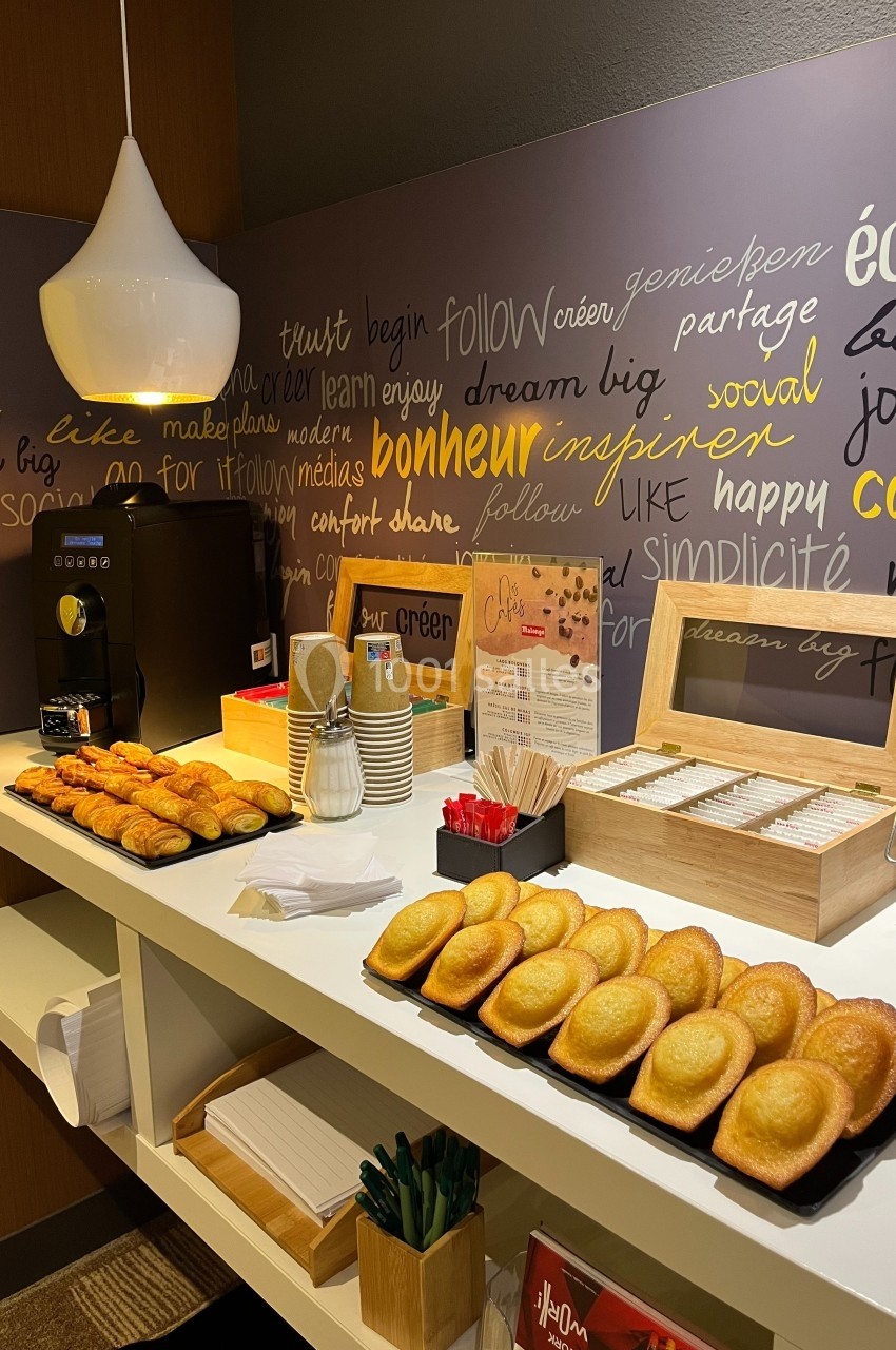 Buffet avec machine à café, viennoiseries, madeleines, sachets de thé et serviettes dans un espace convivial.
