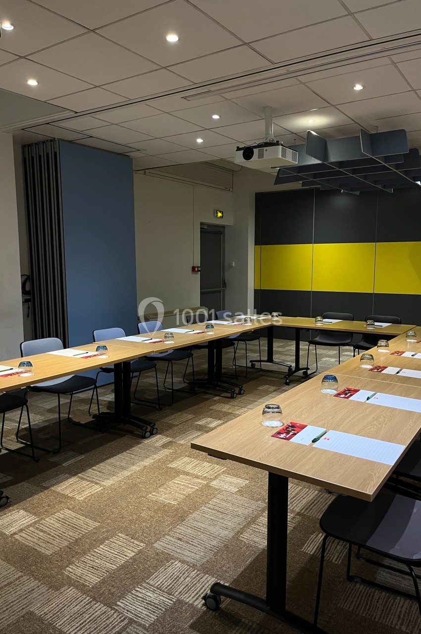 Salle de réunion moderne avec tables en U, chaises, documents et verres disposés pour une présentation ou un atelier.