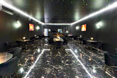 Étagères en verre avec des verres et des bouteilles d'alcool alignés dans un bar au décor sombre.