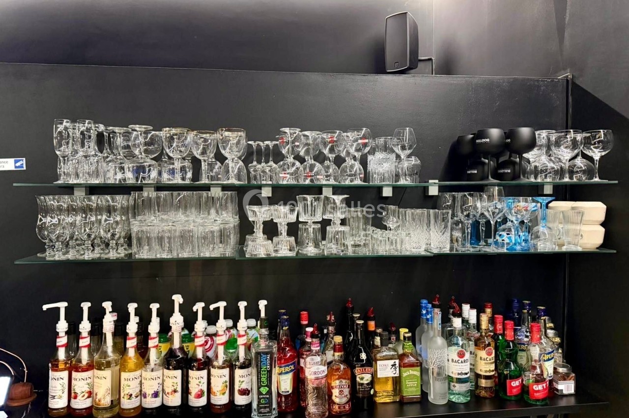 Étagères en verre avec des verres et des bouteilles d'alcool alignés dans un bar au décor sombre.