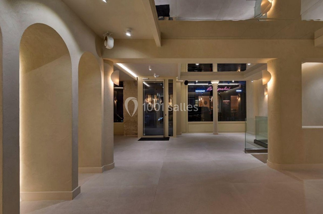 Intérieur d'un espace moderne avec murs beige, arches, éclairage tamisé et grandes fenêtres donnant sur l'extérieur.