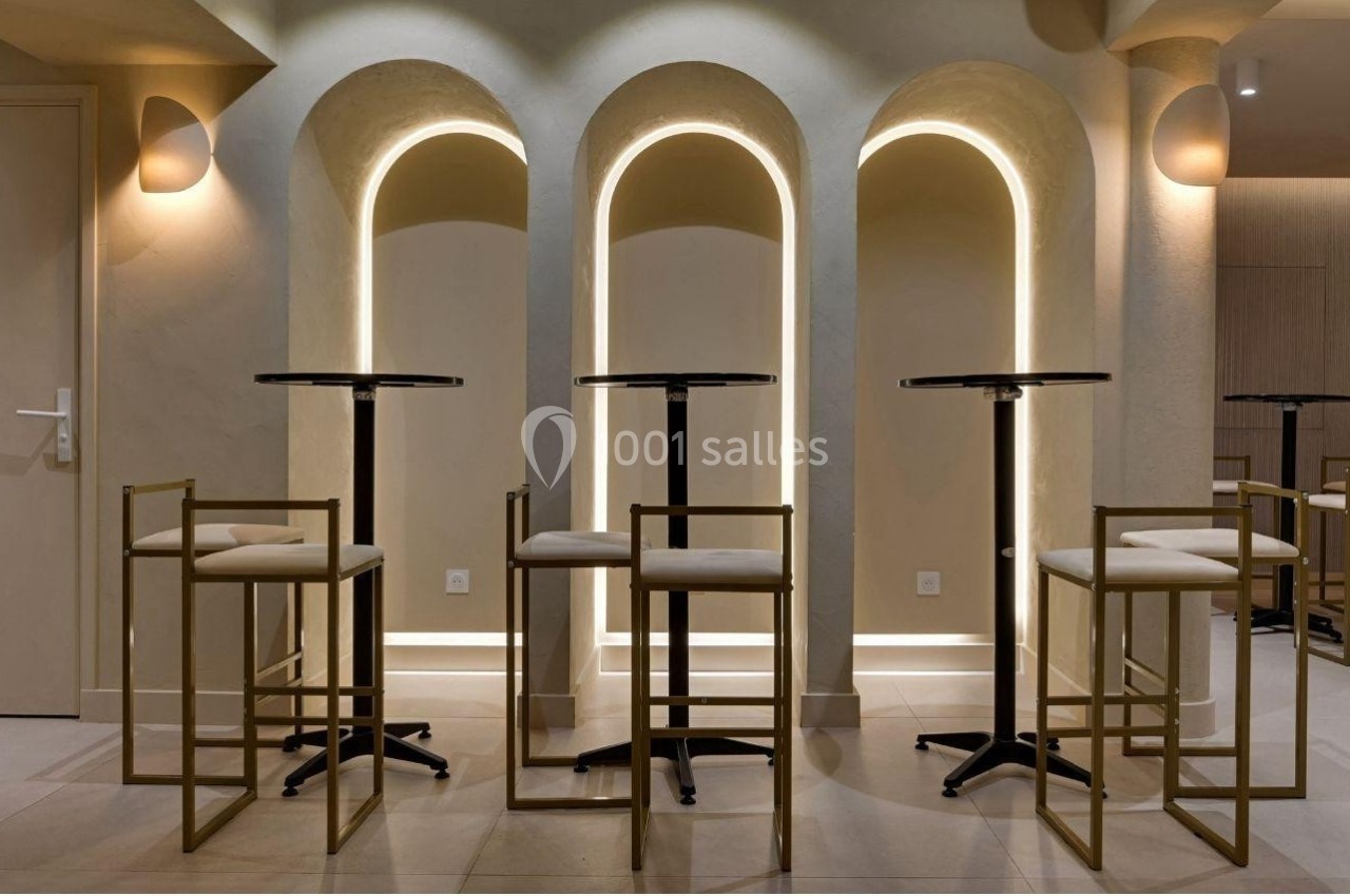 Tables hautes avec tabourets dorés devant des arches lumineuses dans un intérieur moderne et épuré.