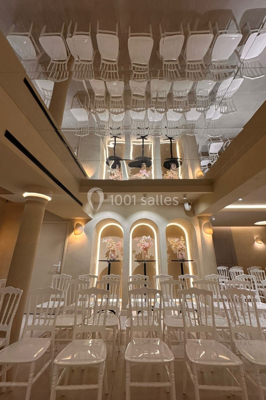 Rangées de chaises blanches alignées dans une salle avec un plafond miroir reflétant l'ensemble de la scène.