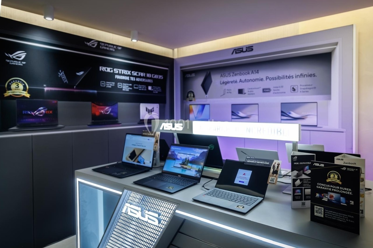 Exposition de plusieurs ordinateurs portables Asus sur un présentoir dans un magasin, avec affiches promotionnelles en…
