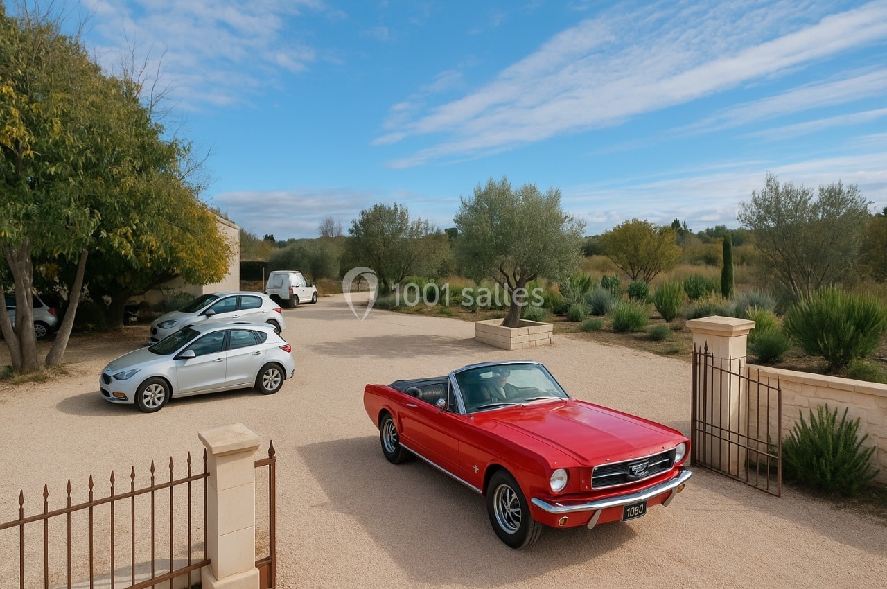 Voiture décapotable rouge garée dans une cour en gravier, entourée de végétation et d'autres véhicules.