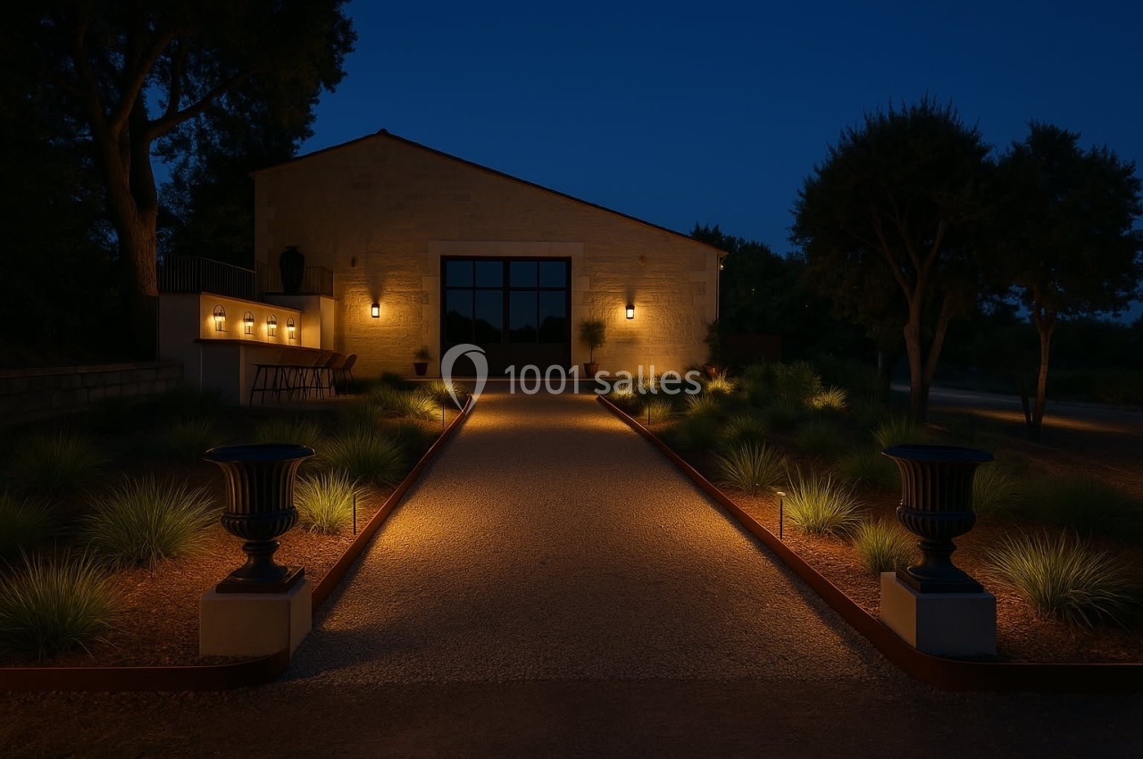 Allée éclairée menant à une maison en pierre, entourée de végétation et illuminée par des appliques murales.