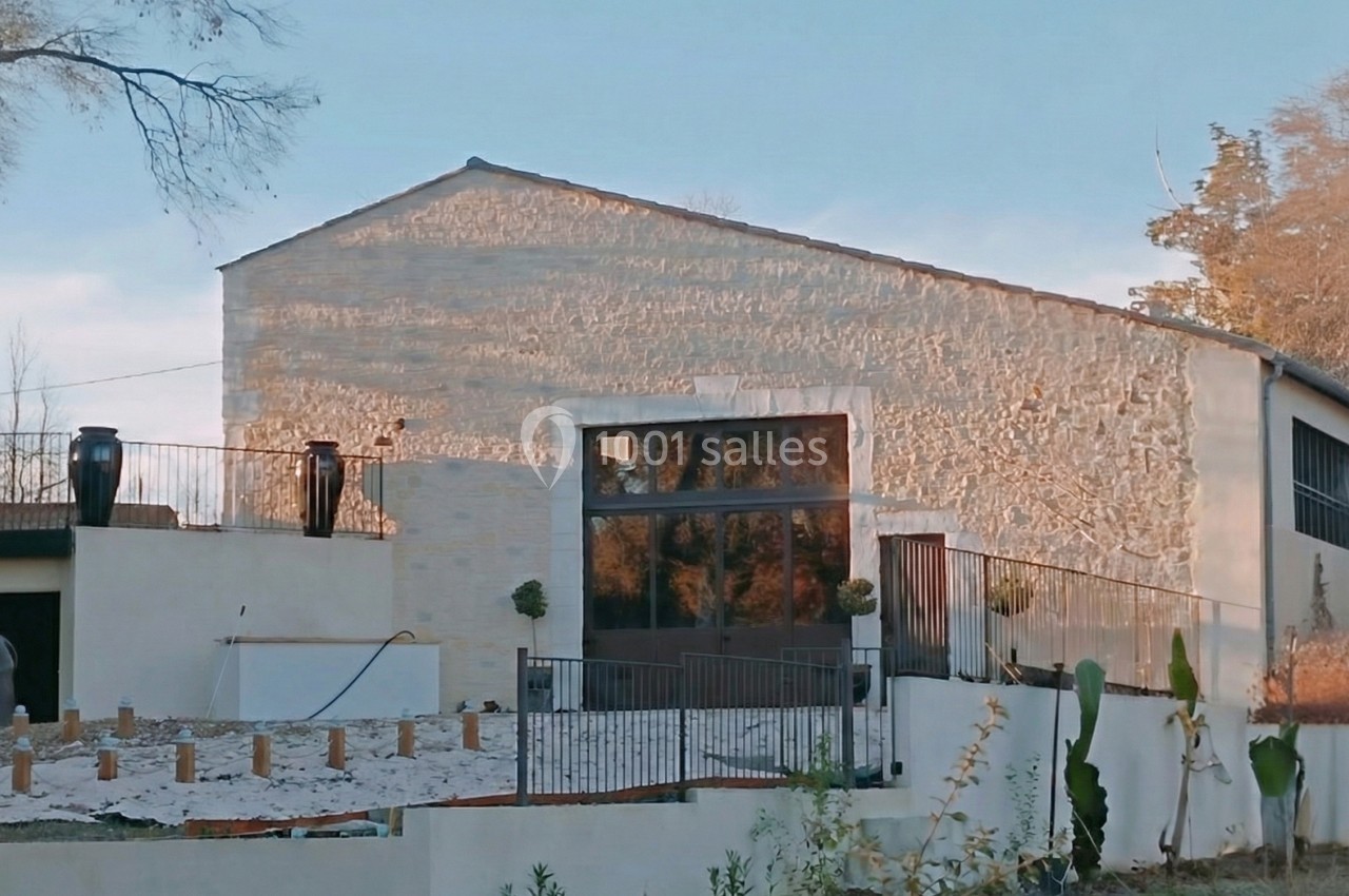 Façade d'un bâtiment en pierre avec une grande baie vitrée, entouré d'une terrasse et de végétation.