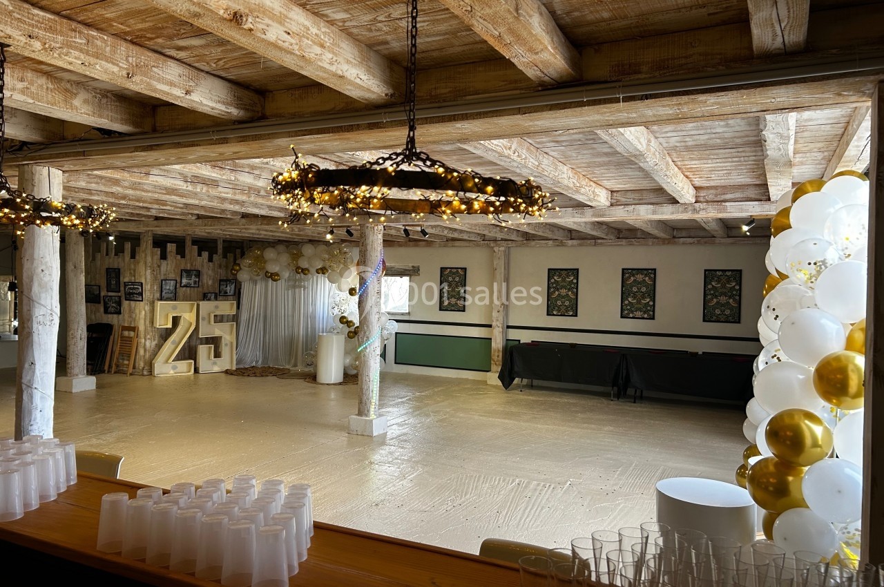 Salle de réception décorée pour un événement, avec guirlandes lumineuses, ballons blancs et dorés, et chiffre 25 lumineux.