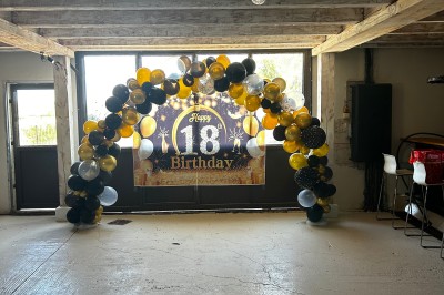 Bannière ’Happy 18th Birthday’ suspendue dans une pièce avec plafond en bois et décorations dorées scintillantes.
