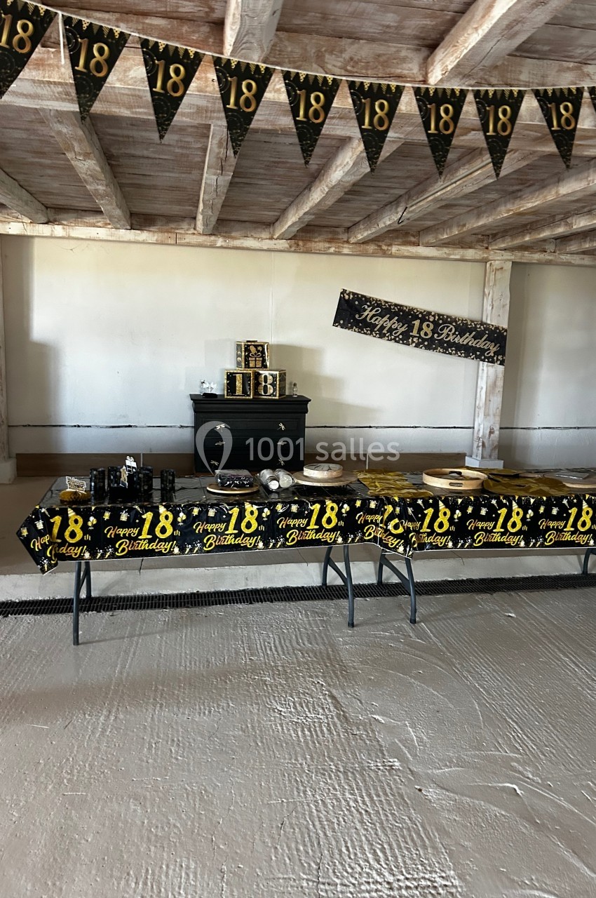 Table décorée pour un 18e anniversaire avec nappes noires et jaunes, guirlandes et bannière assorties dans une salle…