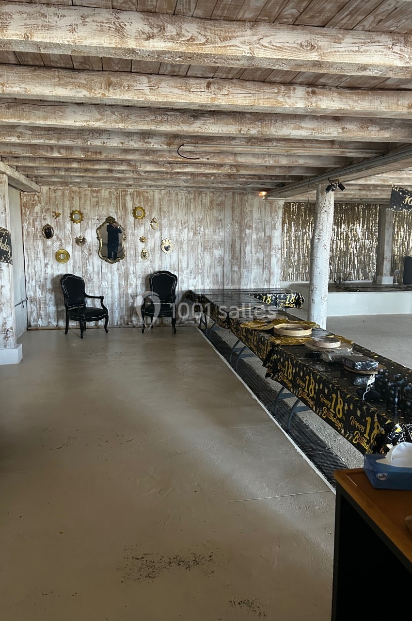 Salle décorée pour un anniversaire, avec une longue table, des chaises noires et des ornements dorés sur un mur en bois.