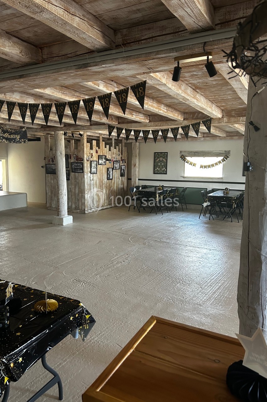 Salle décorée pour un 18e anniversaire, avec guirlandes, tables dressées et poutres en bois apparentes.