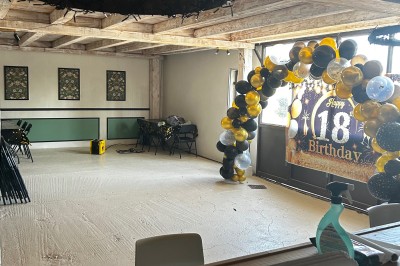 Bannière ’Happy 18th Birthday’ suspendue dans une pièce avec plafond en bois et décorations dorées scintillantes.