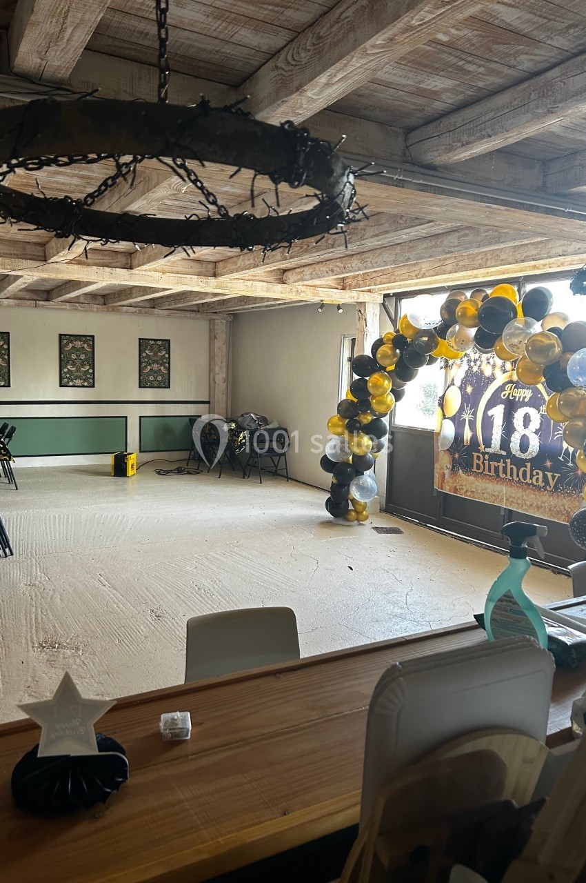 Salle décorée pour un 18e anniversaire avec une arche de ballons noirs et dorés et une banderole festive.