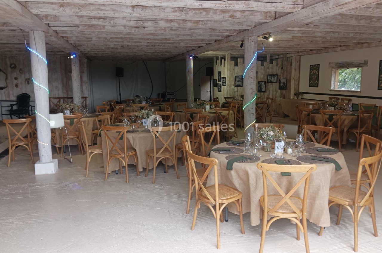 Salle de réception avec tables rondes dressées, nappes en lin beige, chaises en bois et décoration sobre.