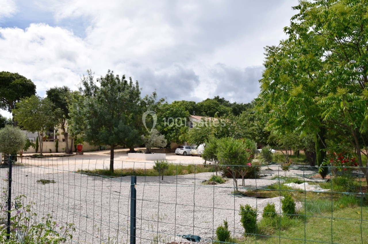 Cour extérieure avec arbres, gravier, végétation et clôture, entourée de bâtiments résidentiels sous un ciel partiellement…