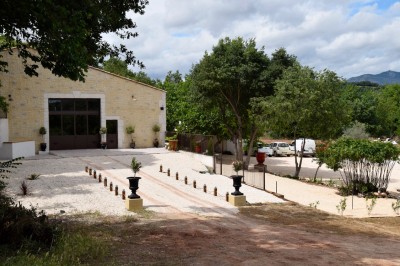 Pot rouge en céramique posé sur un socle en pierre, entouré d'arbres et de gravier dans une cour clôturée.