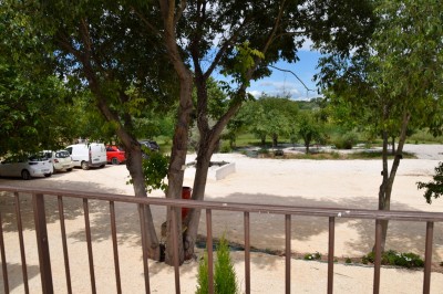 Pot rouge en céramique posé sur un socle en pierre, entouré d'arbres et de gravier dans une cour clôturée.