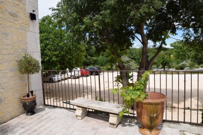 Pot rouge en céramique posé sur un socle en pierre, entouré d'arbres et de gravier dans une cour clôturée.