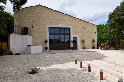 Pot rouge en céramique posé sur un socle en pierre, entouré d'arbres et de gravier dans une cour clôturée.