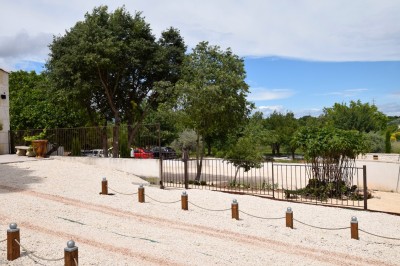 Pot rouge en céramique posé sur un socle en pierre, entouré d'arbres et de gravier dans une cour clôturée.