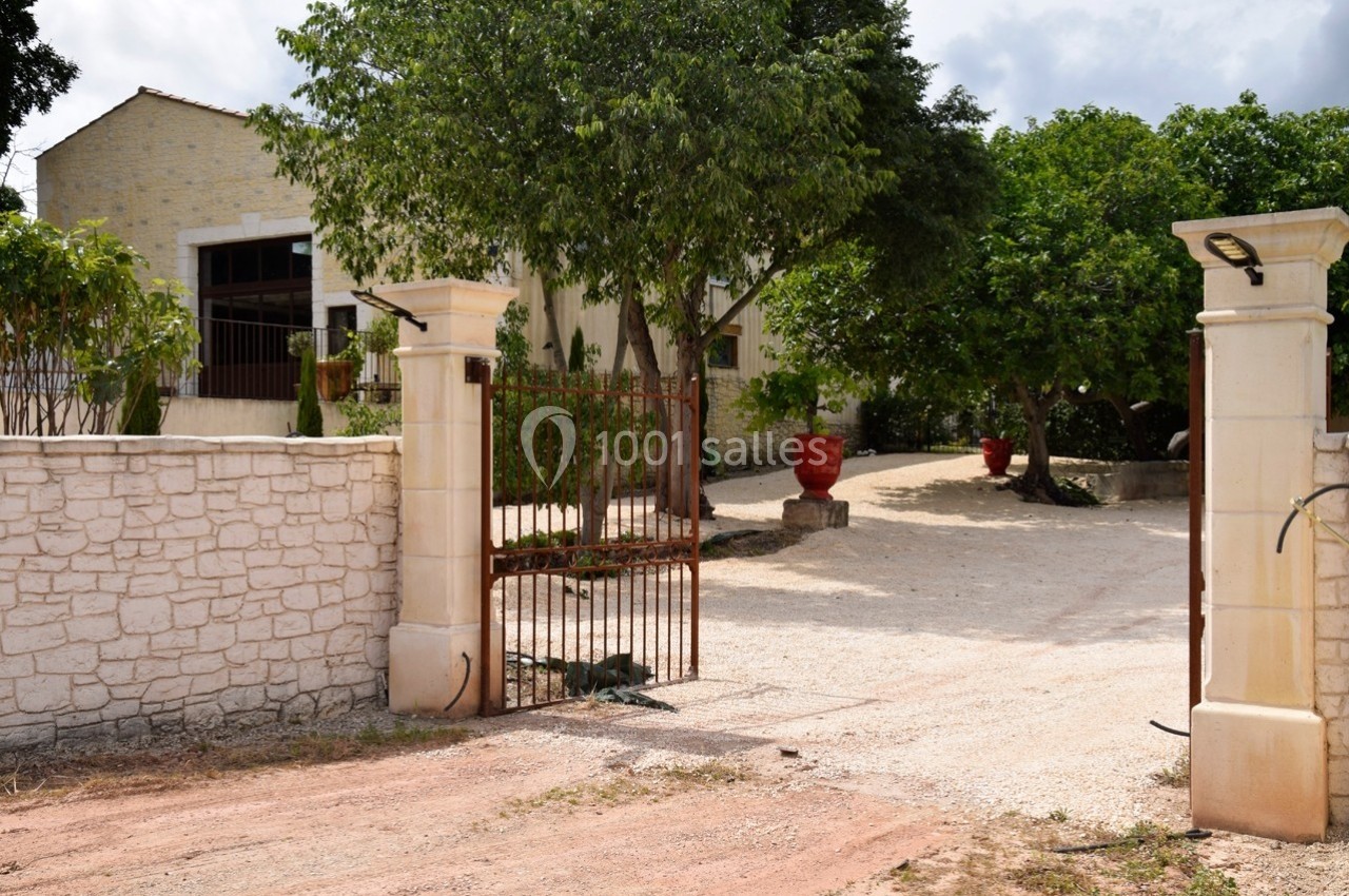 Entrée d'une propriété avec portail ouvert, allée en gravier, murs en pierre et végétation environnante.