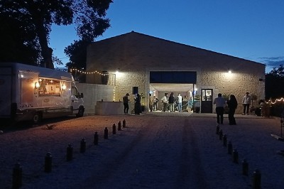 Pot rouge en céramique posé sur un socle en pierre, entouré d'arbres et de gravier dans une cour clôturée.