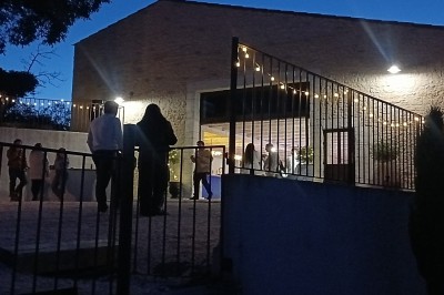 Pot rouge en céramique posé sur un socle en pierre, entouré d'arbres et de gravier dans une cour clôturée.