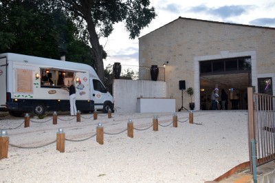 Pot rouge en céramique posé sur un socle en pierre, entouré d'arbres et de gravier dans une cour clôturée.