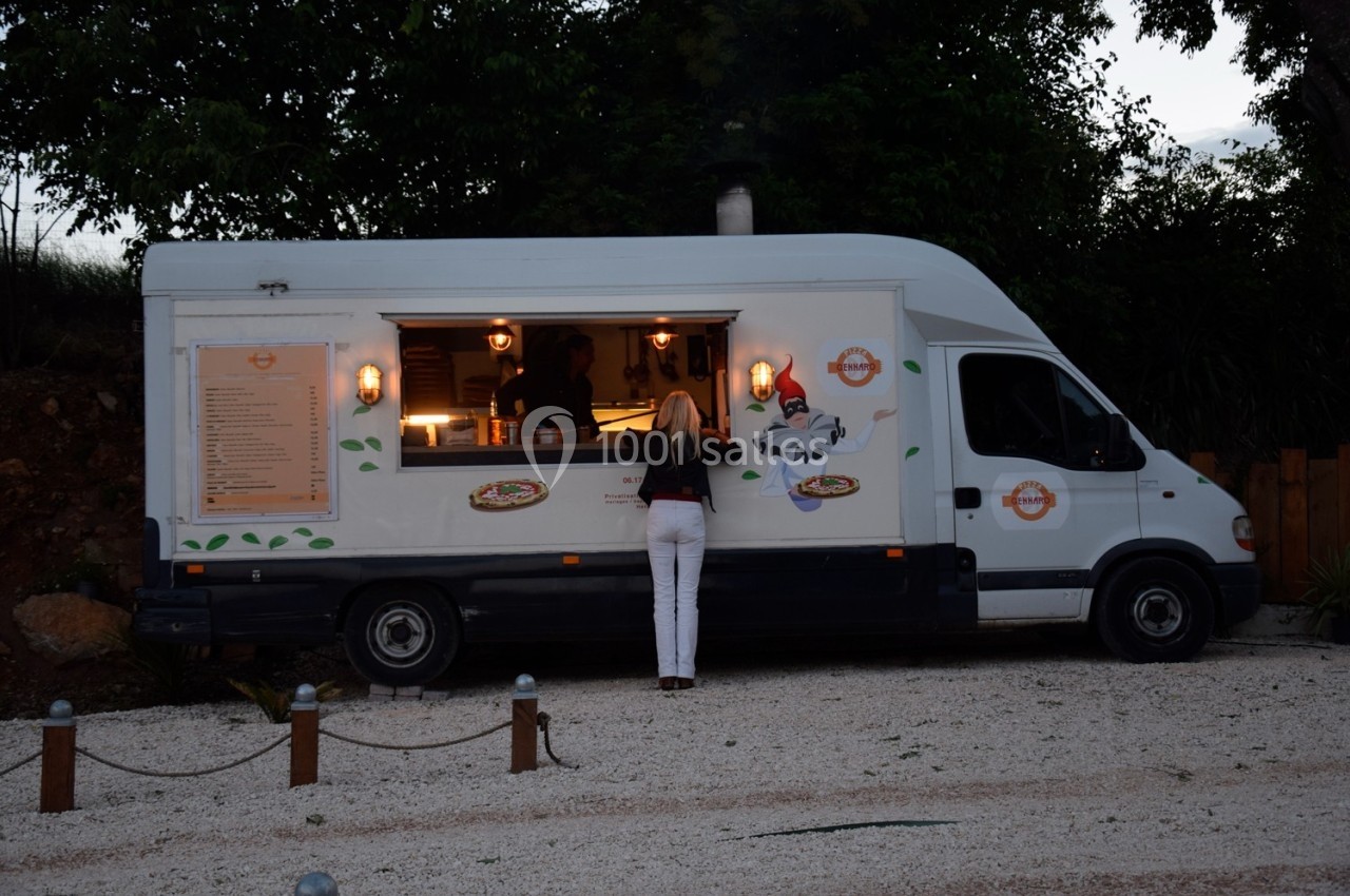 Une femme commande à un food truck blanc stationné sur un parking en soirée.