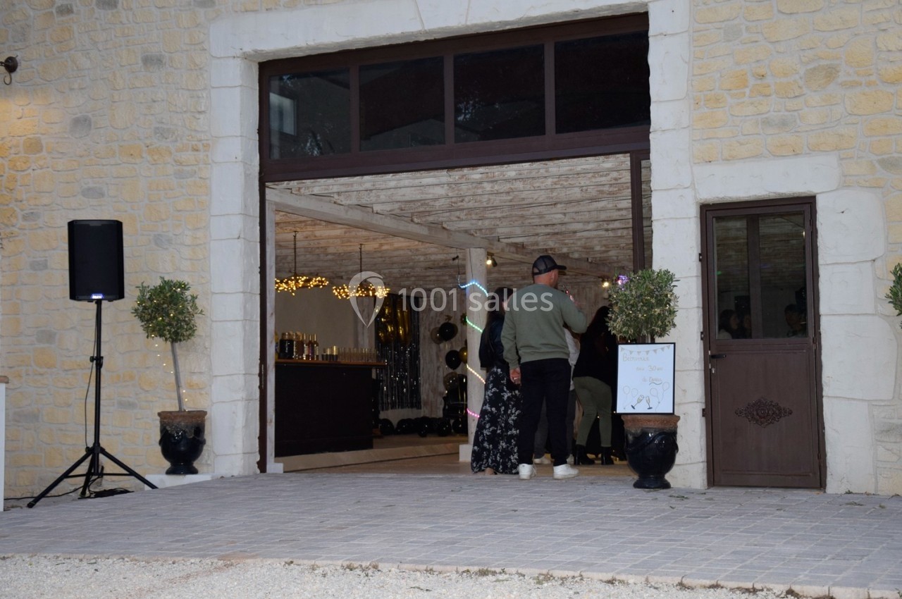 Entrée d'une salle de réception avec des invités debout près d'un bar, décorée de guirlandes lumineuses.