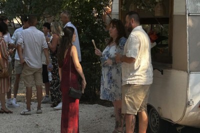 Pot rouge en céramique posé sur un socle en pierre, entouré d'arbres et de gravier dans une cour clôturée.