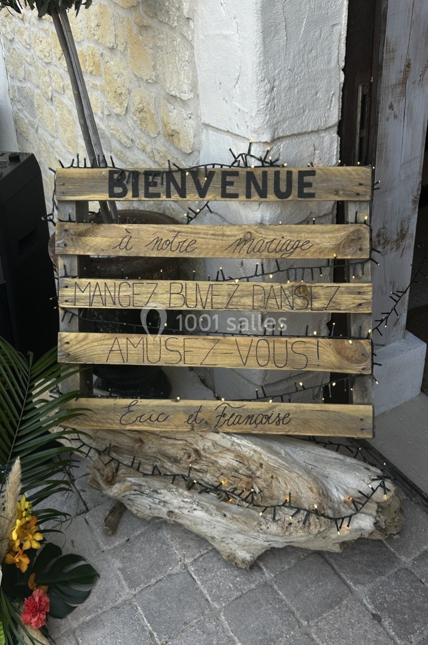 Pancarte en bois avec l'inscription ’Bienvenue à notre mariage, mangez, buvez, dansez, amusez-vous’, décorée de guirlandes.