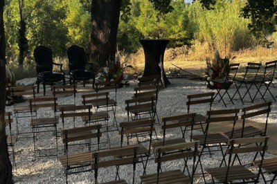 Pot rouge en céramique posé sur un socle en pierre, entouré d'arbres et de gravier dans une cour clôturée.