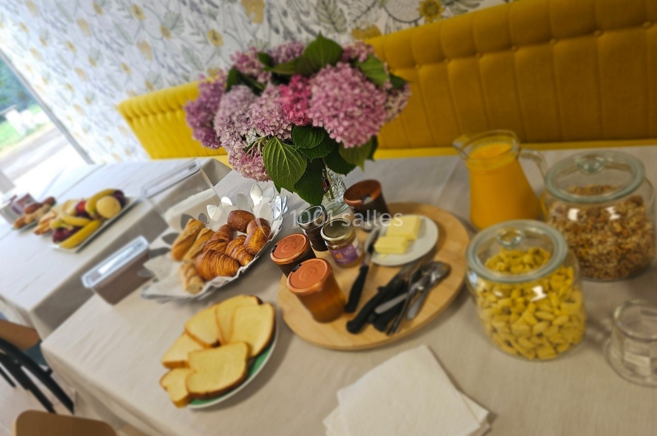 Petit-déjeuner servi sur une table avec viennoiseries, pain, confitures, jus d'orange, céréales et fruits.