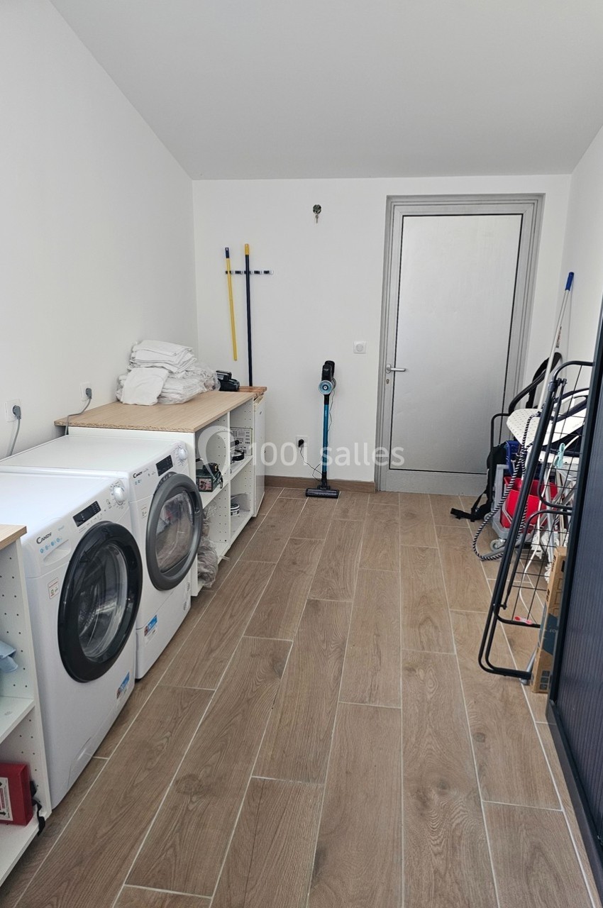 Buanderie avec machines à laver et sécher, étagères de rangement, sols en bois et porte grise au fond.