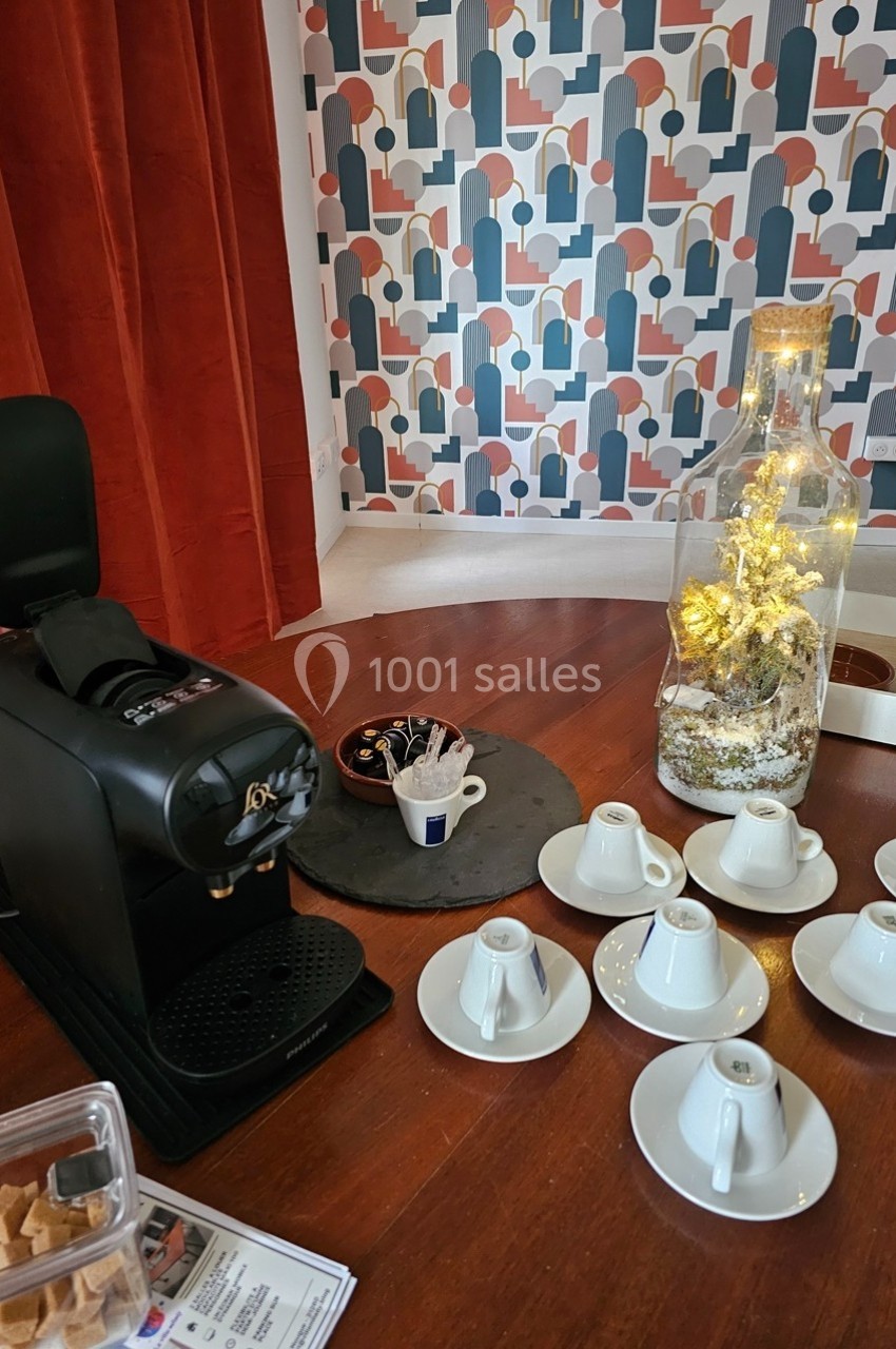 Machine à café avec tasses blanches, sucre et décoration lumineuse sur une table en bois devant un mur à motifs.