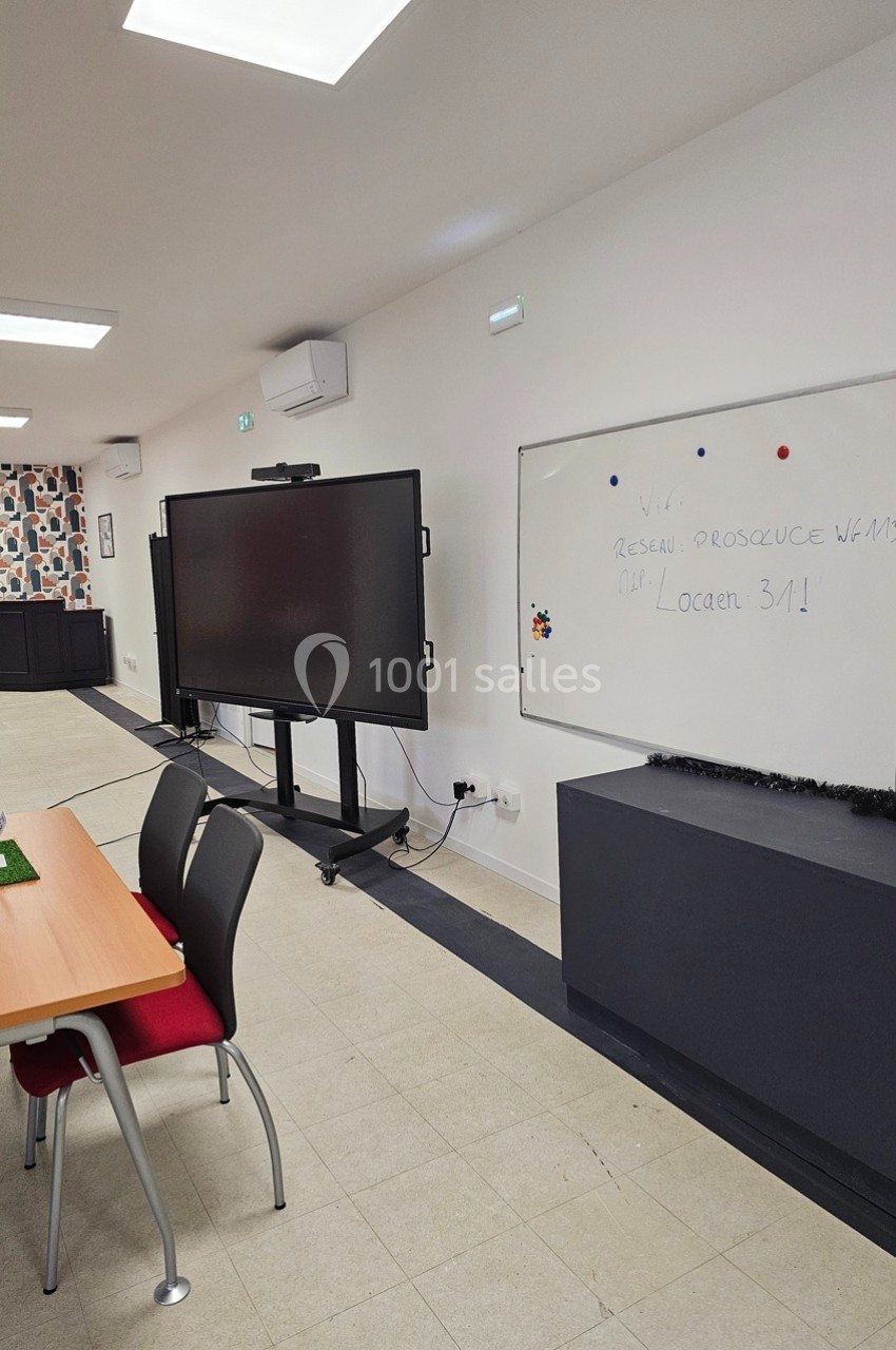 Salle de réunion équipée d'un tableau blanc, d'un écran interactif et de chaises autour d'une table.