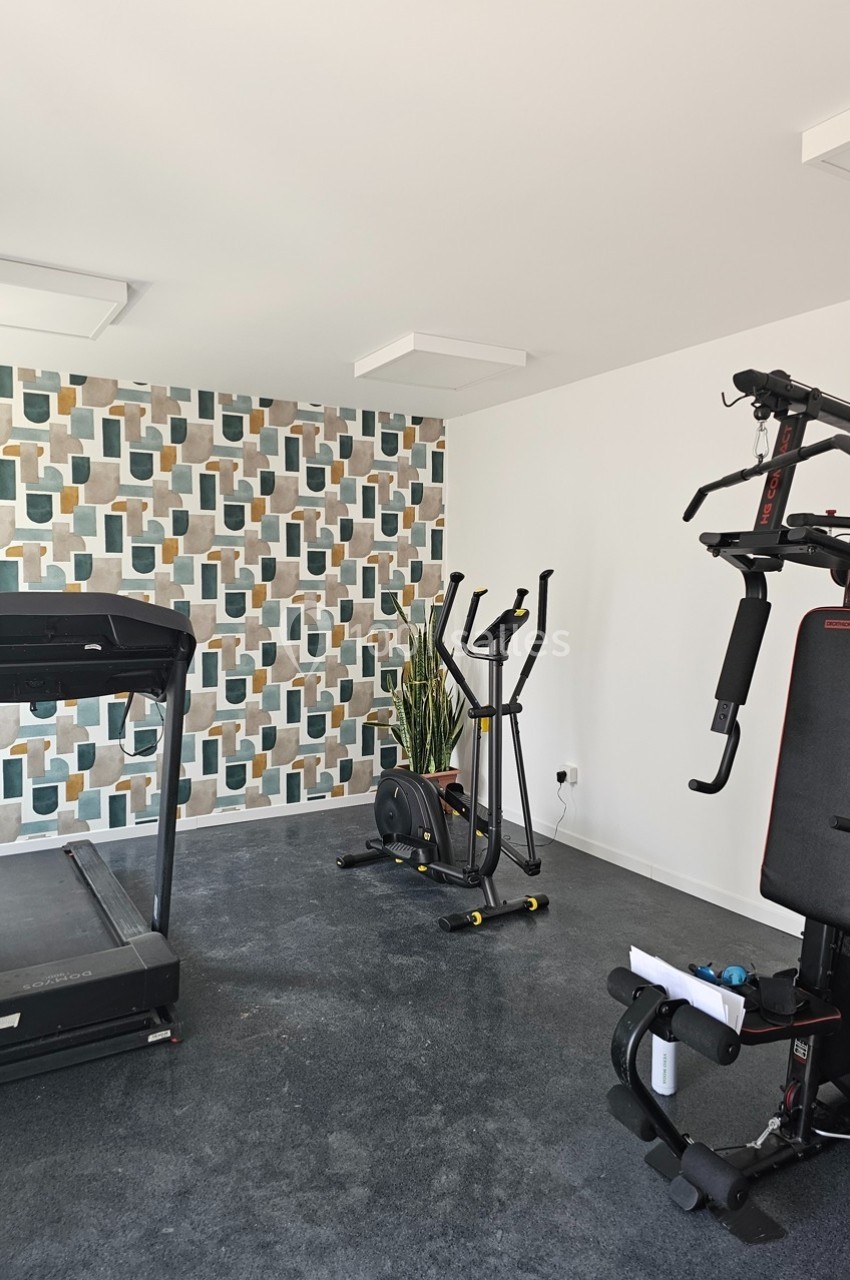 Salle de sport à domicile avec tapis de course, vélo elliptique, appareil de musculation et mur décoratif géométrique.