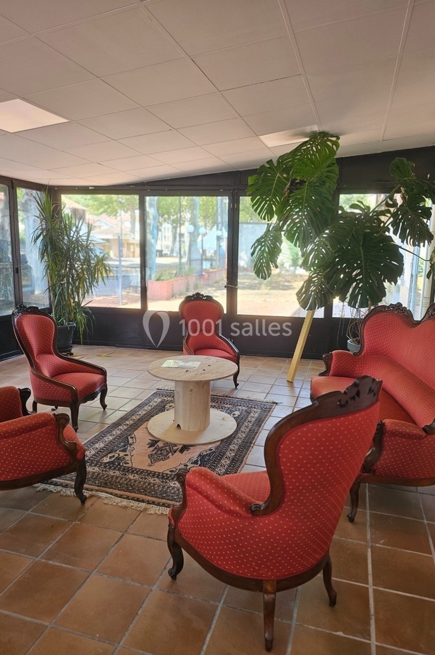 Salon avec fauteuils et canapé rouges, table centrale en marbre, plantes vertes et grandes baies vitrées donnant sur l…