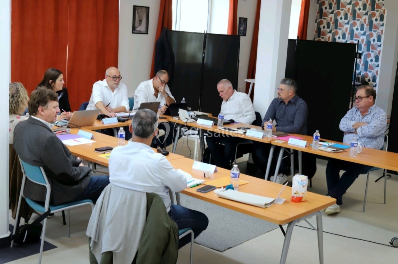 Un groupe de personnes en réunion autour d'une grande table dans une salle lumineuse avec des rideaux rouges.