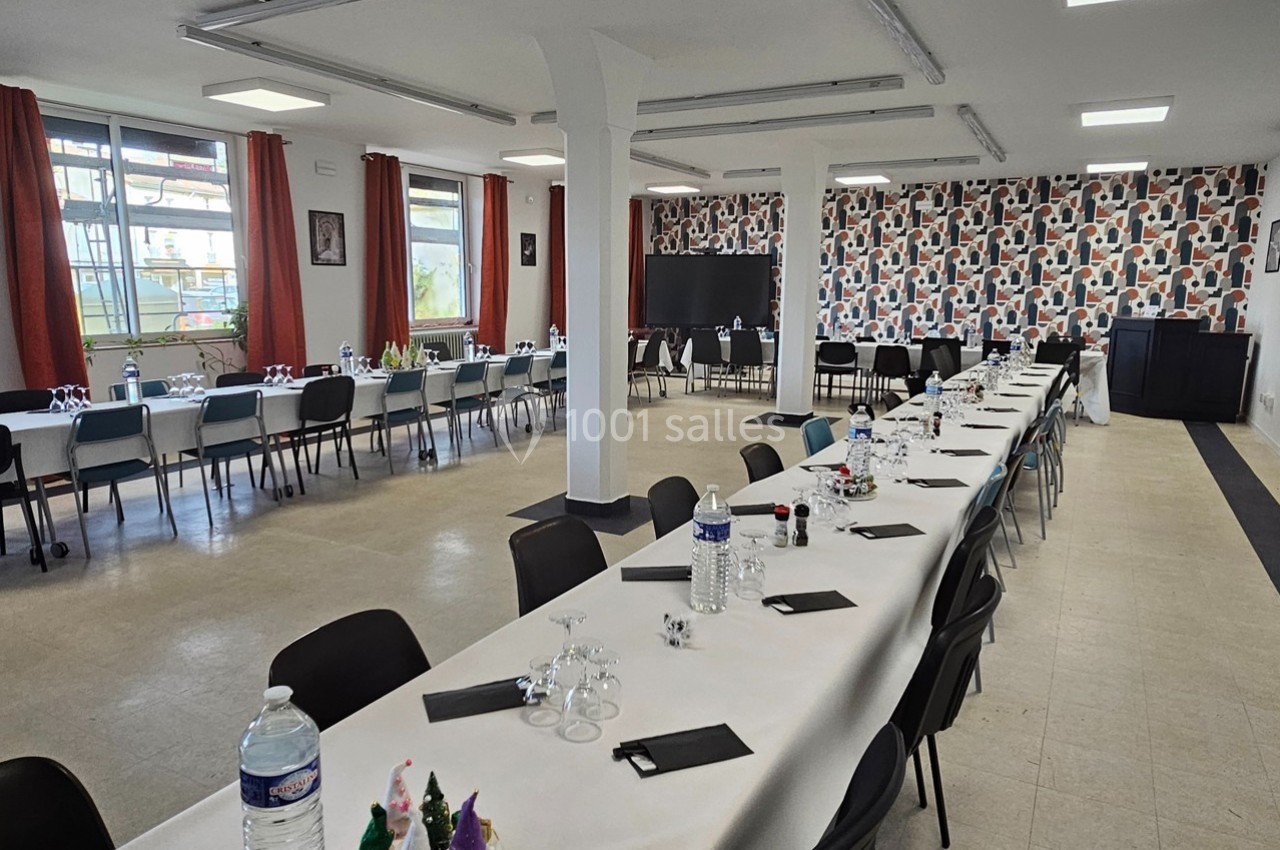 Salle de réception avec de longues tables dressées, décorée de motifs géométriques sur un mur.