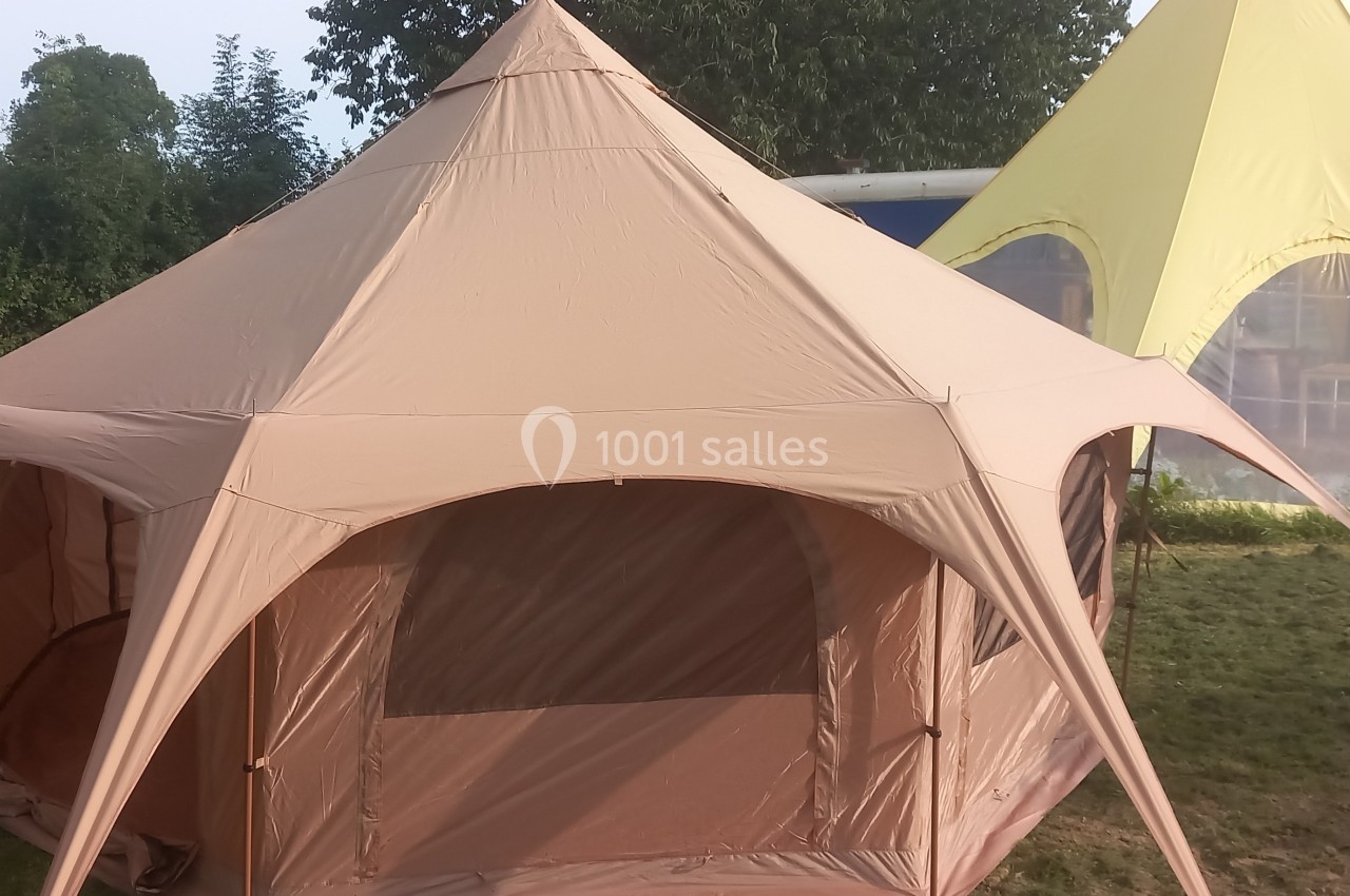 Tente beige à plusieurs pointes montée sur une pelouse, avec une autre tente jaune en arrière-plan.