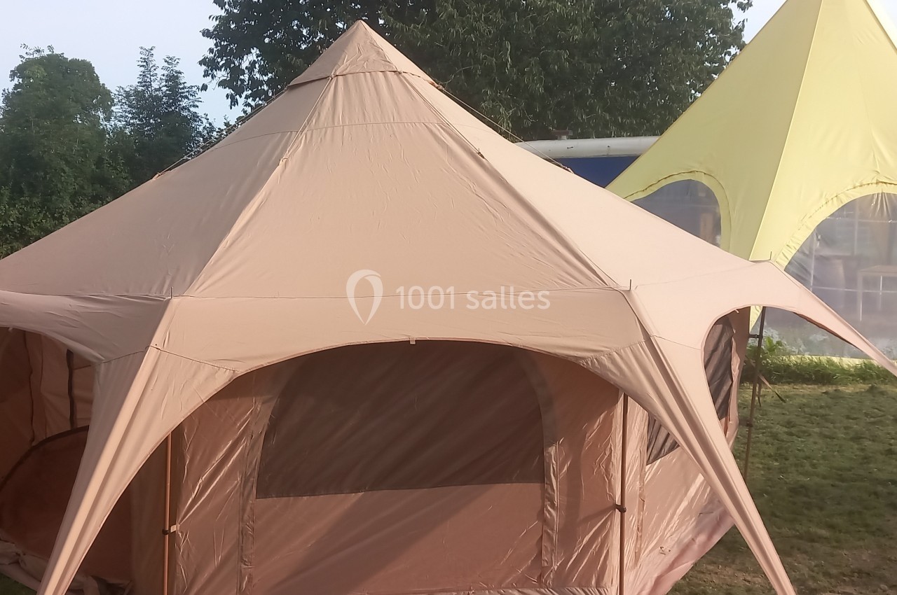 Grande tente beige en toile avec des ouvertures, installée sur une pelouse, à côté d'une tente jaune.