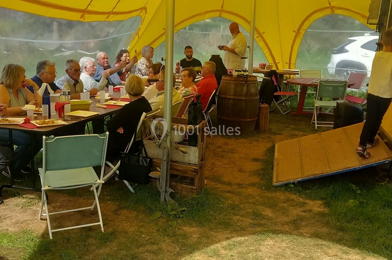 Un groupe de personnes partage un repas sous une tente jaune, près d'une remorque en bois.
